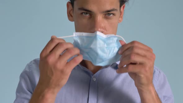 A Handsome Man Demonstrating The Proper Wearing Of Surgical Face Mask Standing Against Light Blue Ba alt