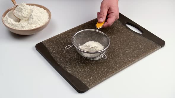 Close-up male hands sifting flour through a sieve on a cutting board