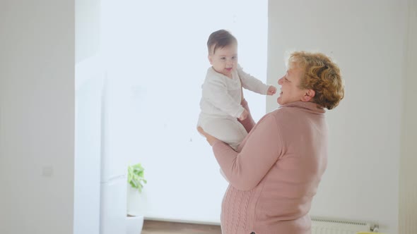 Elderly Woman Holding Her Baby Granddaughter Kiss at Home Young and Old People Together alt