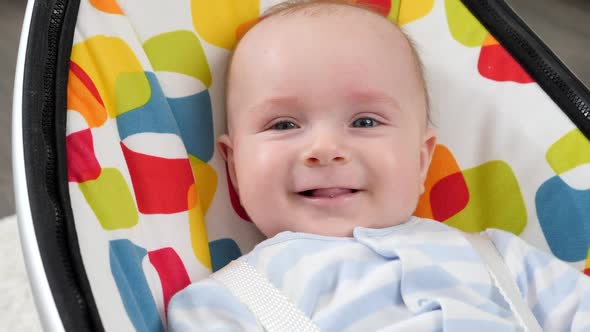 Portrait of Cute Smiling Baby Boy Sitting in Colorful Baby Seat alt