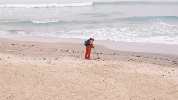 Man with a Metal Detector Walks Along the Beach in a Red Suit