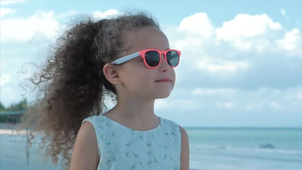 Close-up Portrait of a Beautiful Little Girl in Pink Glasses, Cute Smiling, Looking at the Sea alt