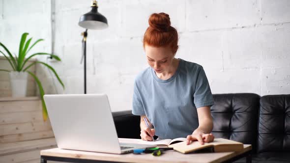 Beautiful Redhead Young Woman Student Is Noting Into the Workbook Important Information From Book. alt