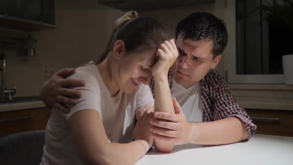 Upset and Stressed Woman Crying and Hugging Her Husband on Kitchen at Night alt