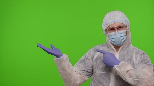 Medical Doctor in Protective PPE Suit Pointing at Left on Blank Space on Chroma Key Background alt