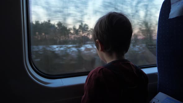 Little boy traveling in train looking outside the window. School holidays ahead.