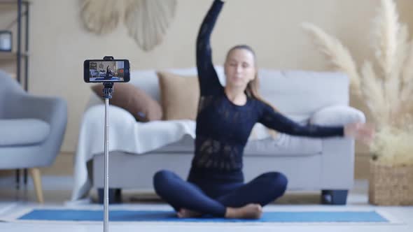 Young Yoga Blogger Woman Streaming Yoga Practice with Cellphone Camera at Home
