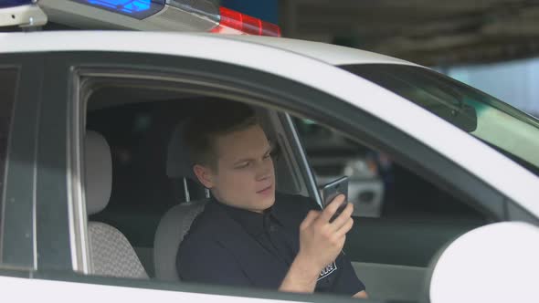 Smiling Policeman in Patrol Car Chatting on Smartphone, Social Network Addiction alt