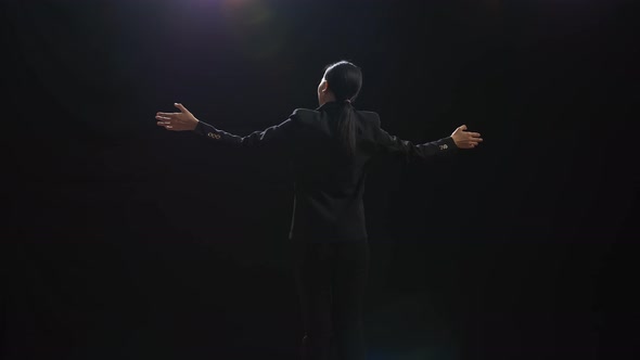 Back View Of Asian Speaker Woman In Business Suit Spreading Out Her Arms In The Black Studio alt