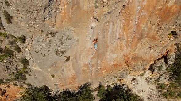 Aerial View From Drone of Strong Muscular Young Man Climbs on Big Rocky Wall By Challenging Rock alt