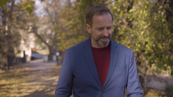 A Middleaged Handsome Caucasian Man Walks and Looks Around in a Park in Fall  Front View