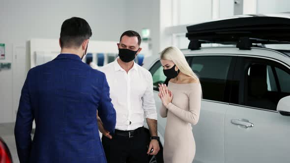 New Car Owners Getting Keys to Purchased Luxury Auto in Dealership Wearing Masks alt