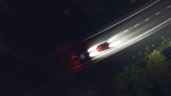 Night scene of a police chase on a curvy road with trees flashed by headlights. alt