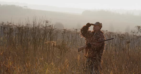 Hunter with Rifle Standing in the Field and Looking Around, Foggy Autumn Morning, Soft Sun Light alt