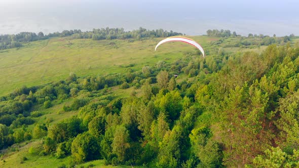 A Person on a Sailwing Is Floating Above the Green Forest alt