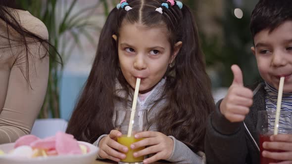 Portrait of Pretty Middle Eastern Girl Drinking Juice Showing Thumb Up with Boy and Unrecognizable alt
