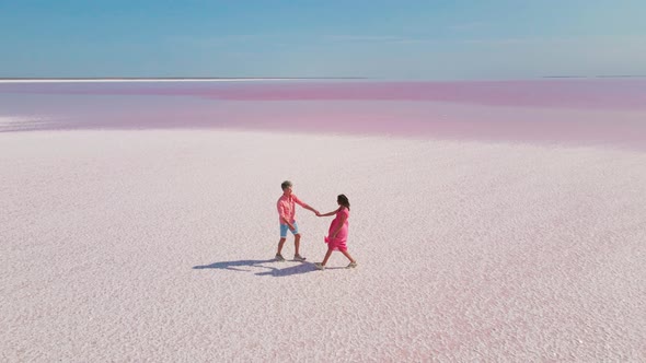Aerial Drone Footage of Happy Young Couple in Pink Wear Having Fun and Joyfully Walking on White alt