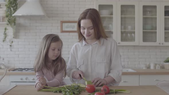 Portrait Pretty Young Smiling Woman Cooking Salad at the Table, Cutting Zucchini. Little Girl alt