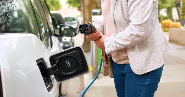 Woman charging electric car at charging station 4k alt