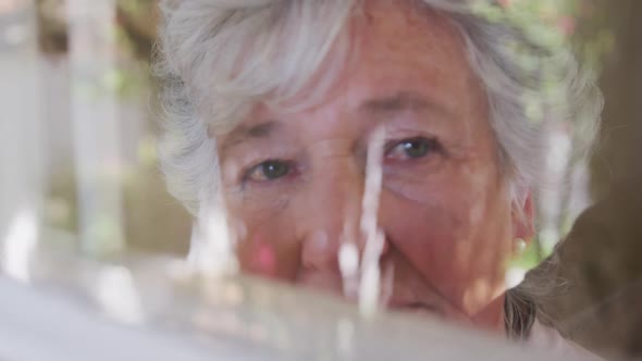 Sad senior caucasian woman looking around seen through window in slow motion alt
