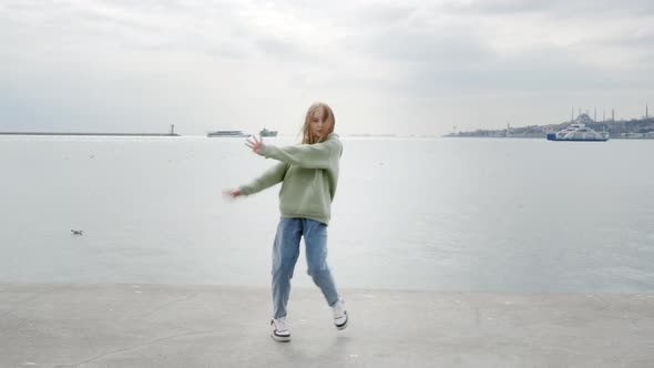 Adorable Teenage Girl Dancing on Embankment with Sea on Background alt