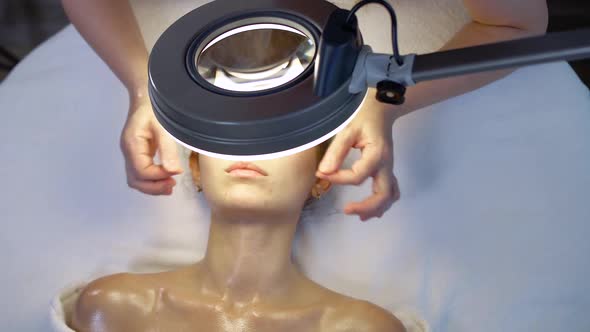Spa and Skin Care the Professional Beautician Looks on the Girl's Face Under the Light of Lamp Skin alt