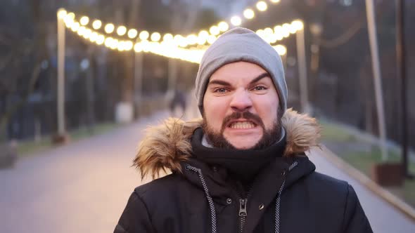 A young man with a beard grimaces at the camera in a winter park alt