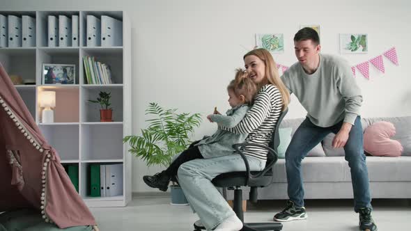 Family Fun Joyful Man Has Fun Rolling Young Woman and Daughter on Chair While Hanging Out Together alt