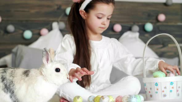 Girl playing with rabbit and easter eggs on the bed alt