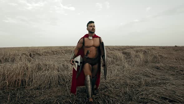 Shirtless Spartan Walking in Dry Field. alt