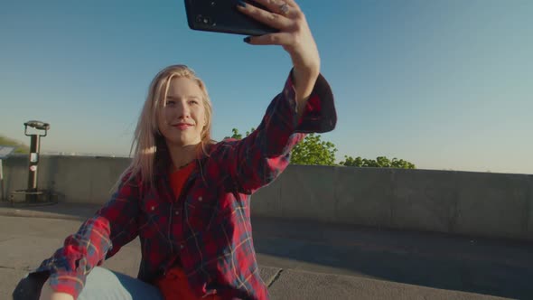 Cool Female Skateboarder on Skateboard Making Selfie at Daybreak alt