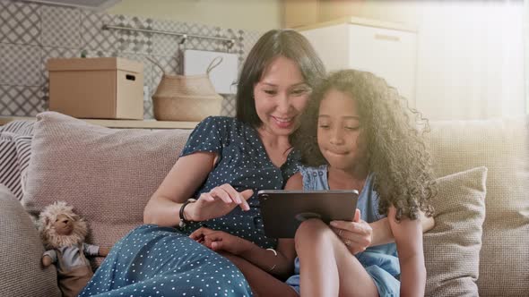 Mother and Daughter Having Fun on a Digital Tablet in a Home Interior. A Cute Happy Mother and alt