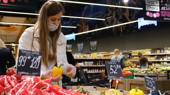 Woman in a protective mask in the supermarket buys oranges. alt