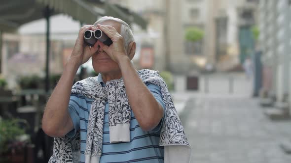 Senior Man Tourist Exploring Town. Looking in Binoculars. Travel Lviv, Ukraine alt