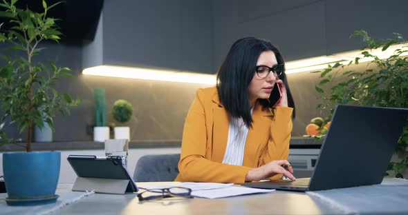 Brunette in Business Clothes in Glasses Talking on Mobile while Working at Home alt