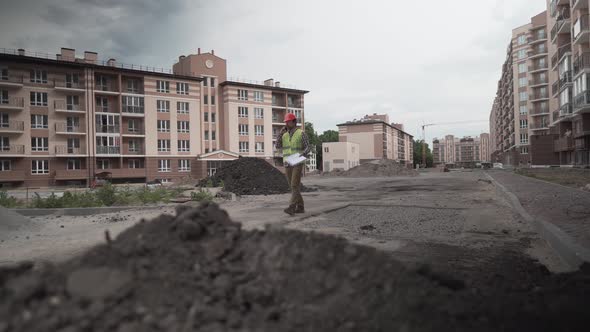 Builder in Protective Work Clothing Walks Through Construction of Houses Talking on Phone with alt