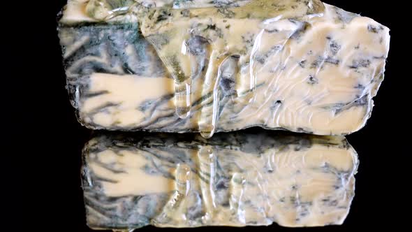 Drops of honey flowing down from the Dorblu cheese on a mirrored black background. alt