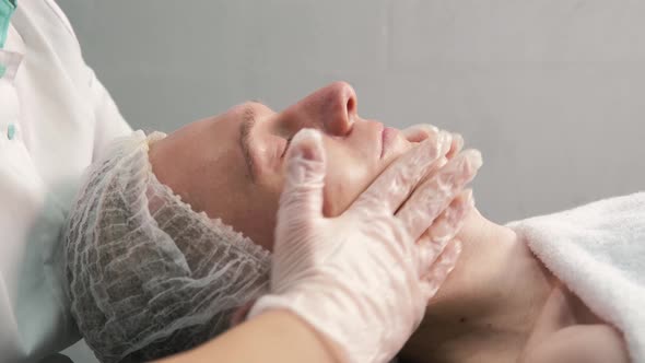 A Cosmetologist with Gloved Hands Gives a Facial Massage to a Young Man