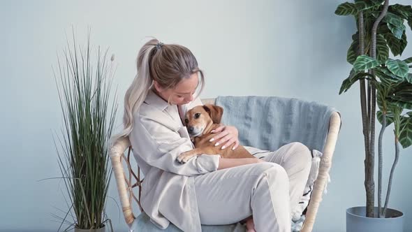 Young Beautiful Blonde Woman Caucasian Nationality Home Clothes Sits in a Cozy Armchair Hugging Her alt