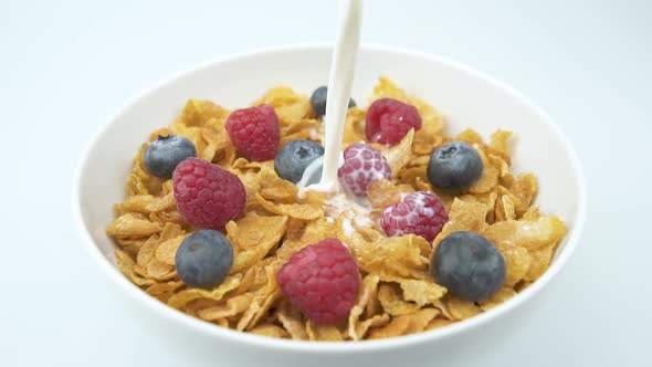 Pouring Milk Into Corn Flakes With Raspberry In A Bowl