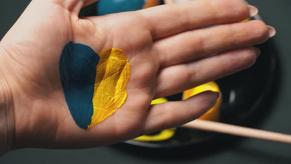 Painted Female Hand in YellowBlue Color on the Background of Easter Eggs alt