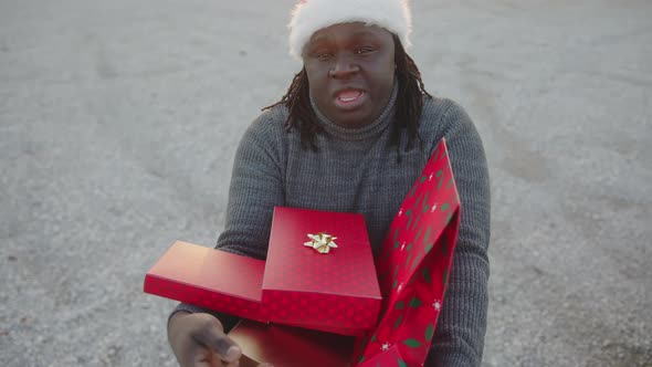 Black Man with Santa Hat Holding Bunch of Red Wrapped Christmas Presents alt