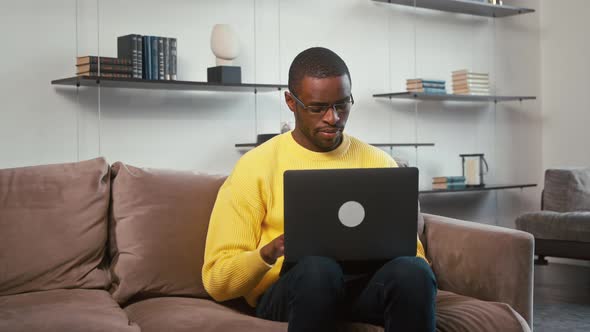 Young man working with laptop on the couch at home. A man with a laptop on the couch alt
