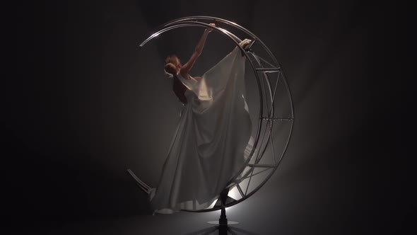 Gymnast Performs the Splits in a White Dress on a Rotating Design. Smoke Background alt