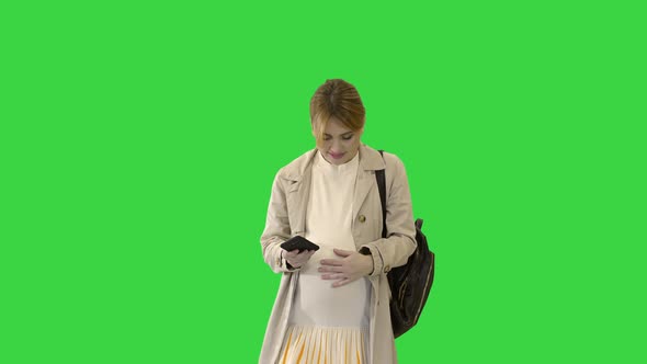 Pregnant Girl with Phone in Hand Walking on a Green Screen, Chroma Key. alt