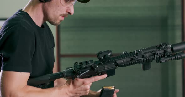 A Man Loads a Magazine Clip Onto a Rifle and Fires a Round at an Indoor Firing Range alt