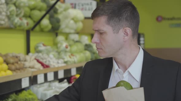 Close-up of Confident Adult Caucasian Man Choosing Pomelo in Grocery, Putting Citrus Fruits Into alt