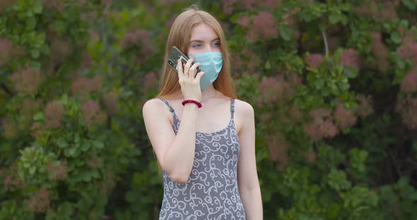 Beautiful young girl, blonde, in a protective medical mask talking on the phone