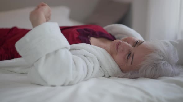 Beautiful Mature Woman Lying in Bed Stretching and Smiling Looking at Camera alt