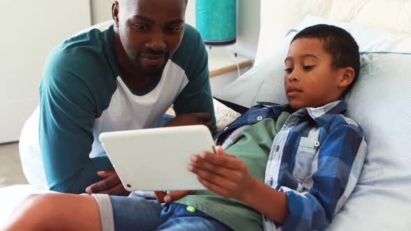 Son showing digital tablet to his father in bedroom alt
